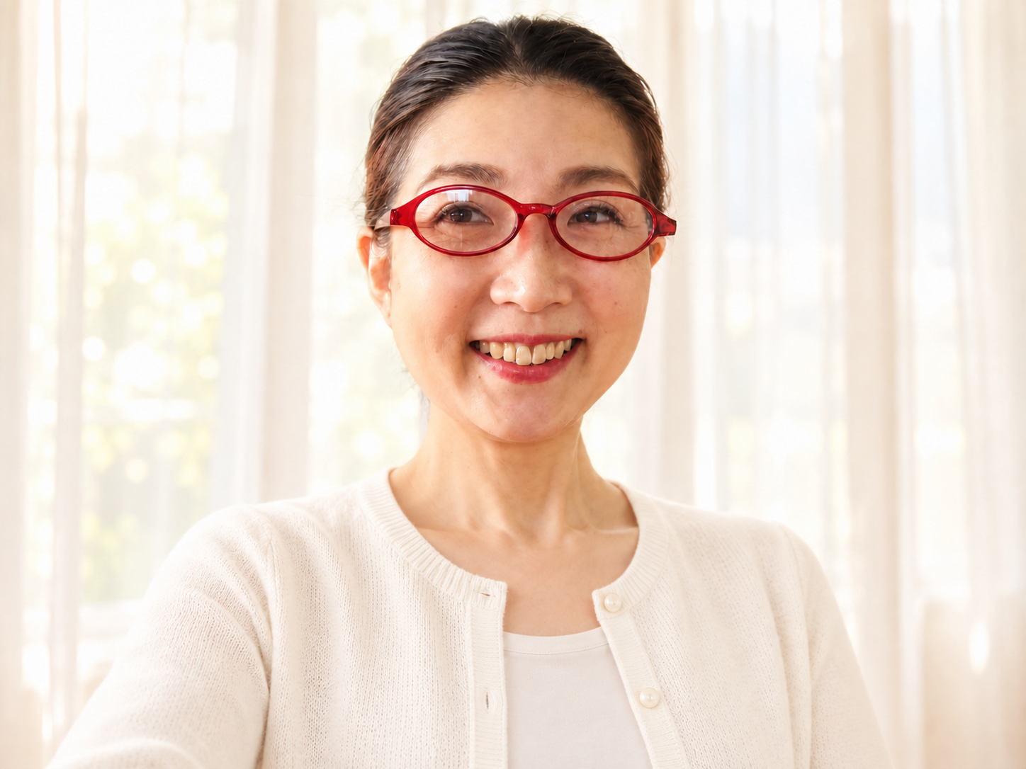 白いカーディガン姿で、薄いカーテン越しの自然光の中で微笑む布恵さん